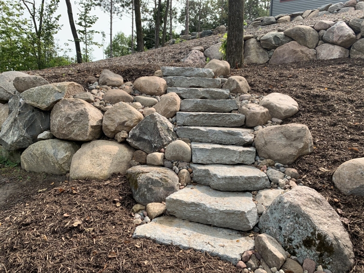 Stone staircase built into fieldstone boulder retaining wall with boulder outcroppings.