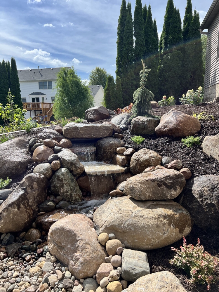 Beautiful fieldstone pond-less waterfall with colorful perennials and shrubs make this truly the backyard oasis