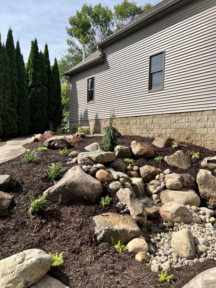 Beautiful fieldstone pond-less waterfall with colorful perennials and shrubs make this truly the backyard oasis