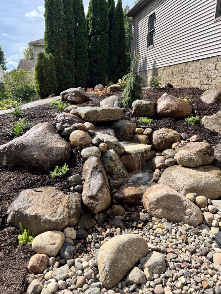 Beautiful fieldstone pond-less waterfall with colorful perennials and shrubs make this truly the backyard oasis