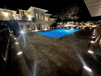 Night view of large slab paver pool deck with lighting.