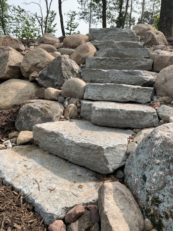 Stone staircase built into fieldstone boulder retaining wall with boulder outcroppings.