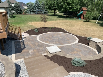 Large slab 5- piece paver patio with circle patio inlay and seating wall with pillars and block staircase.