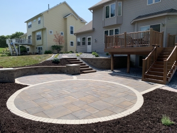 Large slab 5- piece paver patio with circle patio inlay and seating wall with pillars and block staircase.