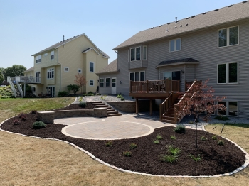 Large slab 5- piece paver patio with circle patio inlay and seating wall with pillars and block staircase.