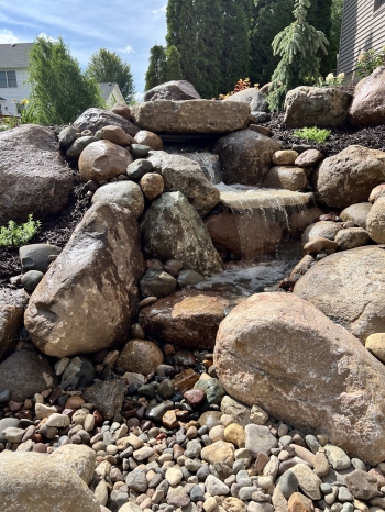 Beautiful fieldstone pond-less waterfall with colorful perennials and shrubs make this truly the backyard oasis